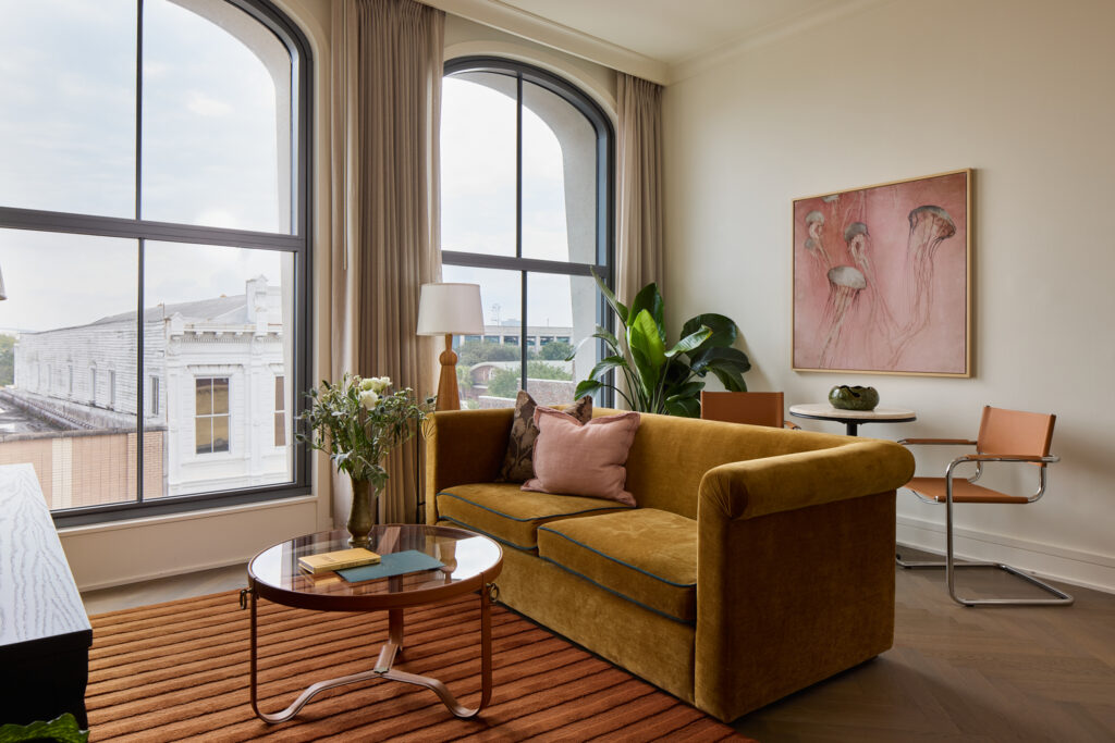 Ochre velvet sofa beneath arched windows in a King Street hotel suite designed by Method Co.