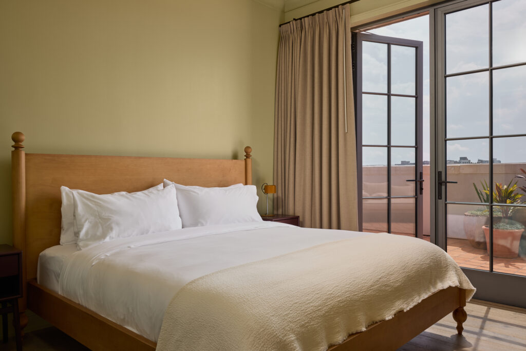 Rattan headboard and crisp white bedding in a light-filled guest room at The Nickel Hotel