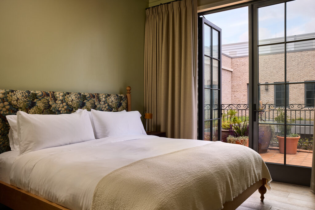Guest room with botanical headboard and wrought-iron balcony overlooking Upper King Street