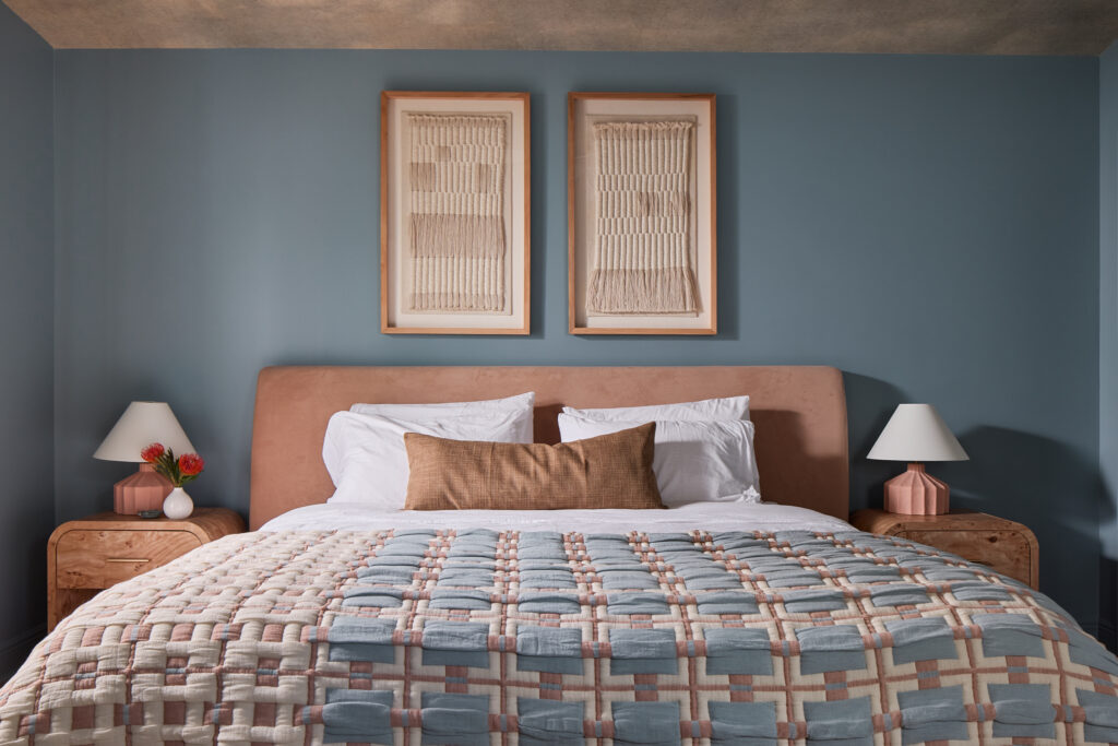 Dusty blue bedroom with coral upholstered bed, patterned quilt and framed art in a Charleston Airbnb