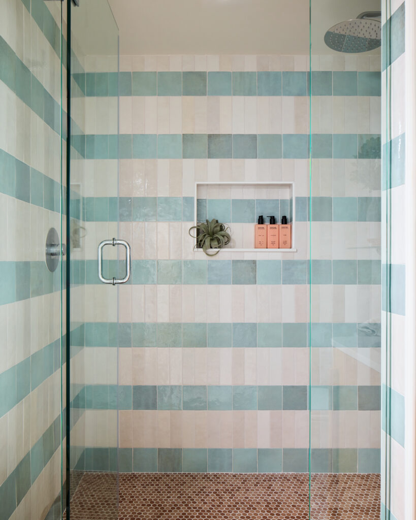 Aqua and white striped tile shower with built-in niche in a Charleston vacation rental